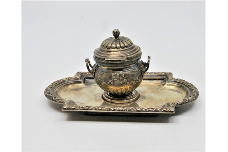 Tinteiro em prata relevada e assente sobre bandeja com frisos e volutas, alma de vidro no interior.